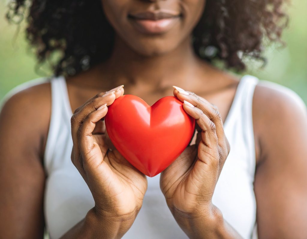 African American woman holding a red heart symbol, representing heart health and wellness