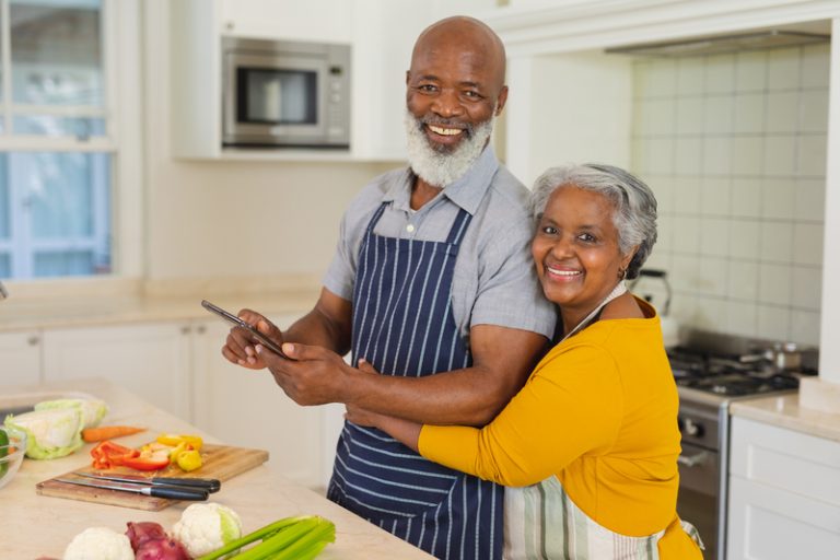 Older African American couple smiling while participating in a community-based nutrition class featuring culturally relevant recipes and food demonstrations.