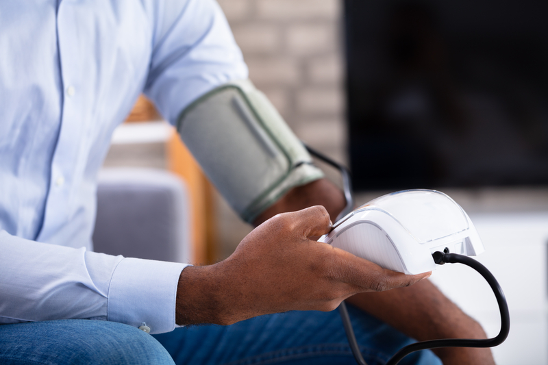 Middle-aged African American man checking his blood pressure at a community health clinic as part of heart disease prevention and awareness.