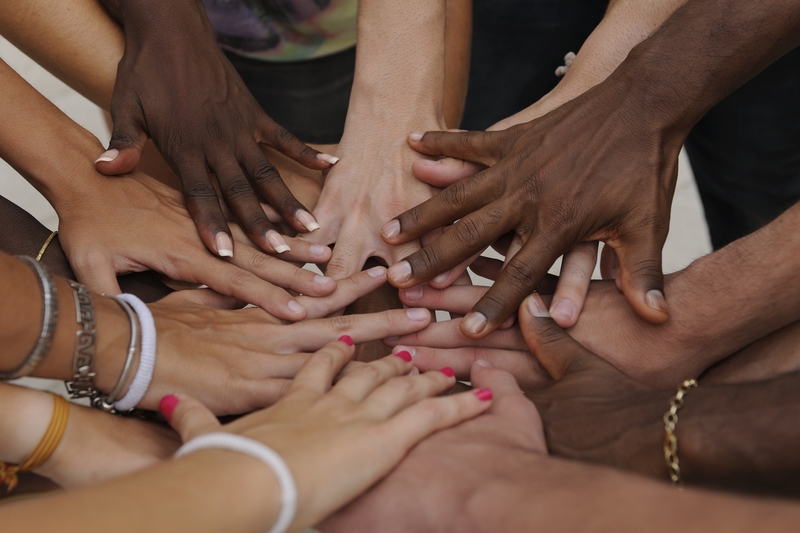Diverse group of people placing their hands together, representing metastatic breast cancer support and community.