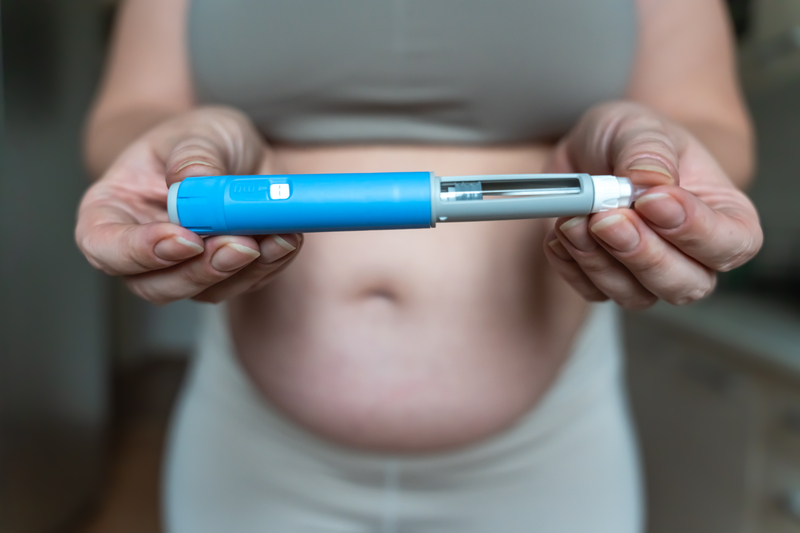Woman holding a GLP-1 injection pen as employers reconsider weight-loss drug coverage